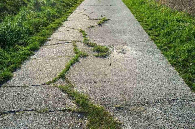 Cracked and damaged concrete driveway with visible wear and weeds growing through the surface in Columbia Station, OH